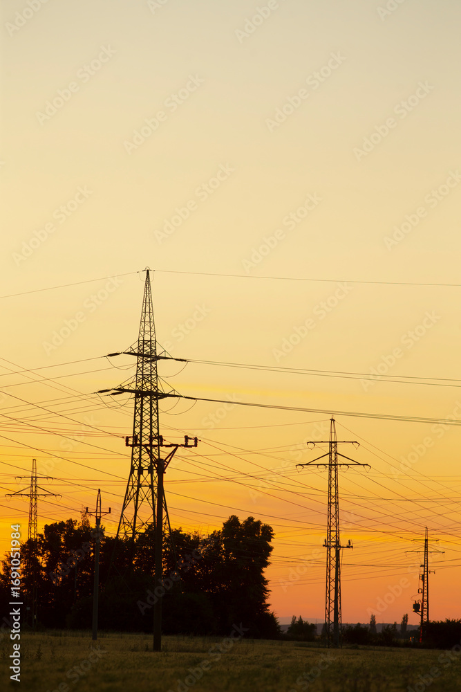 Fototapeta premium Silhouettes of electricity transmission towers against a vibrant sunset sky, illustrating energy infrastructure in a serene landscape.