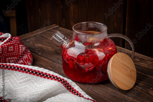 Hot berry fruit tea with fresh raspberry, lemon slices and herbs served in transparent glass teapot on rustic wooden table