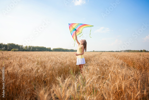 A beautiful girl runs with a kite on the field. A beautiful young woman with a flying multicolored kite over a clear blue sky. Free, the concept of freedom. Emotions, healthy lifestyle