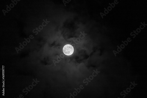Full moon in the dark night sky with clouds, natural background.