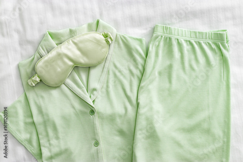 Pajama Set with silk sleep mask pastel green colored on white sheet. Top view fashion woman home sleepwear from natural cotton on bedclothes. Cozy pyjamas of shirt and shorts for comfort dream