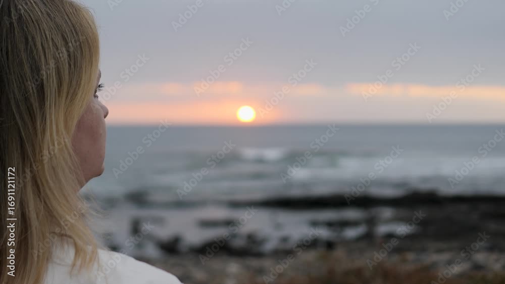 A woman is enjoying a breathtaking sunset view by the ocean shore A woman is enjoying a breathtaking sunset view by the ocean shore