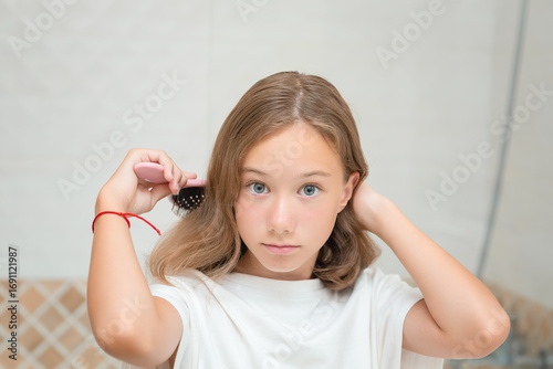 A pretty little girl with big blue eyes and a comb in her hand. The child combs unruly hair. Cute little girl is playing with a hairbrush.
