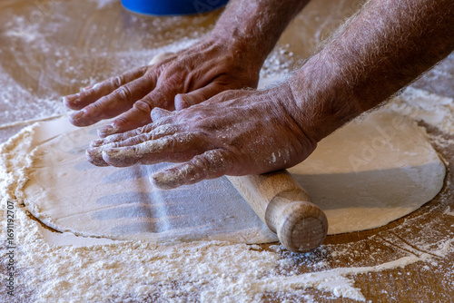 A close up of a mans hands rolling out pizza dough on a table