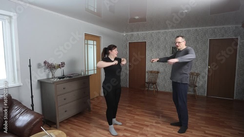 Doing light exercise at home, middle aged white woman in sportswear and mature man in homewear smiling together.