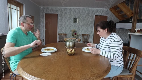 Family couple eats pumpkin soup with croutons at dining table enjoying cozy meal together in warm home atmosphere.