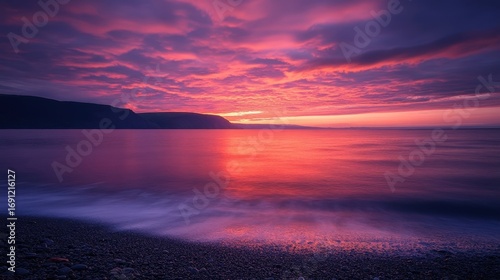 Stunning sunset over calm ocean waves and purple clouds at dusk, creating a serene and beautiful coastal scene.
