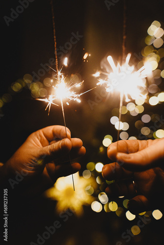 Happy New Year! Burning sparklers in hands on background of christmas tree golden lights bokeh at night. Glowing fireworks in couple hands, new year eve holiday celebration