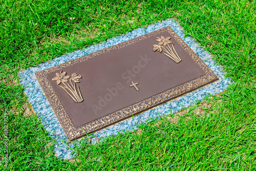 Photography Bronze memorial marker with floral engravings cross rests on peaceful cemetery