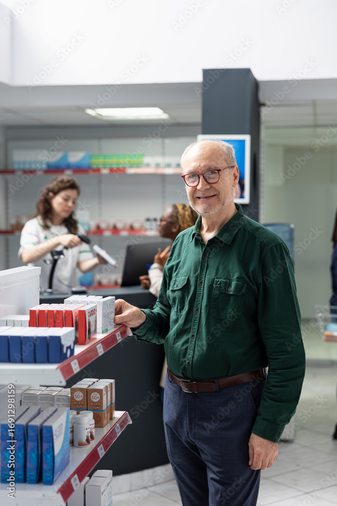 Fototapeta premium Portrait of senior man drugstore customer checking healthcare products on shelves, reading labels on medical supplies in the pharmacy shop. Self care support and wellbeing in a drugstore.
