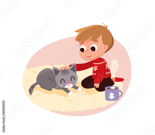 A little boy wearing a Christmas sweater sitting on the floor, rug petting his kitten. Cup of hot chocolate with marshmallows  beside him, nearby.