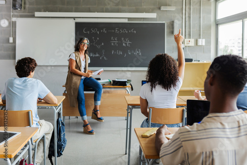 Fotografi Rear view of young high school student girl raising her hand to ask a question in class