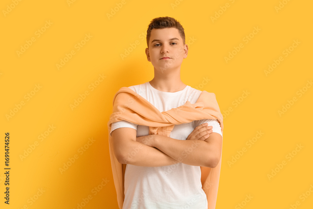 Obraz premium Confident young boy with folded arms and casual style on bright yellow background, youthful expression and modern fashion