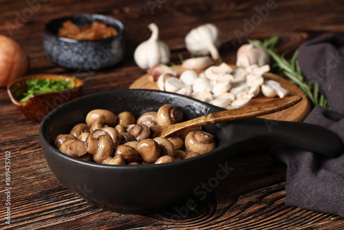 Frying pan with roasted mushrooms, garlic and rosemary on wooden background