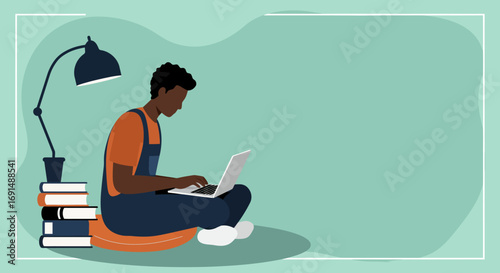 Focused young African American man uses a laptop for remote work or online study, surrounded by books. Concept of digital learning and productivity.