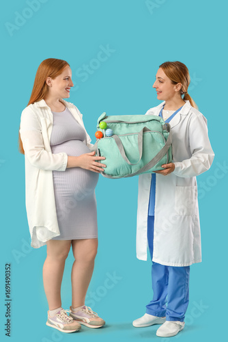 Young pregnant woman and doctor with maternal hospital bag on blue background