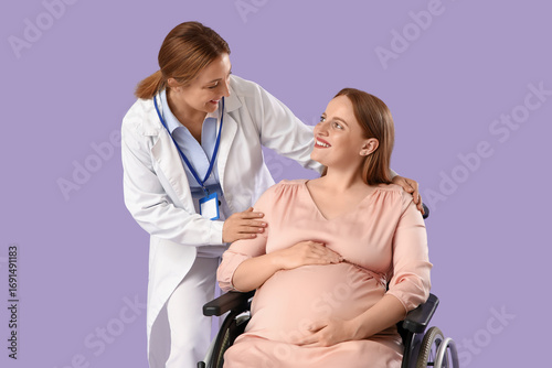 Young pregnant woman in wheelchair with doctor on lilac background