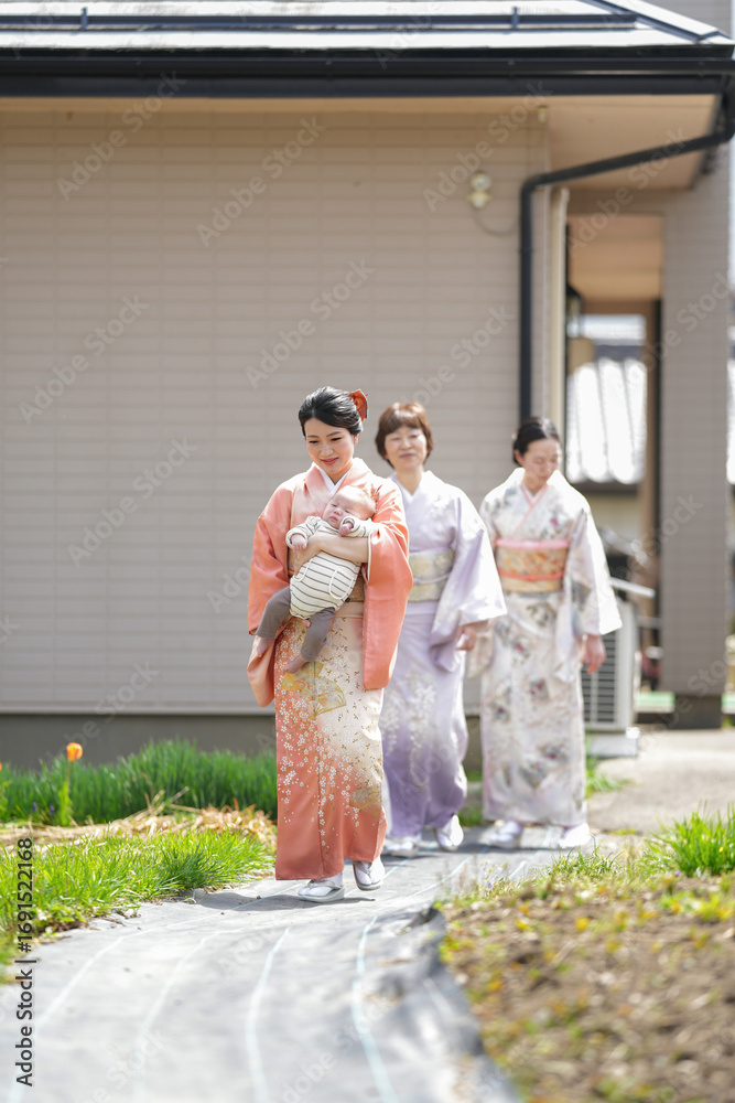 Fototapeta premium Three women in traditional Japanese clothing walk down a path. One of the women is holding a baby