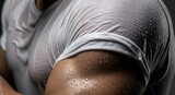 Close-up of a muscular man's arm and shoulder, with a wet white t-shirt clinging to his body, showing sweat and exertion.