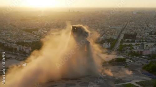 Building demolition at sunset, dust and debris filling the air