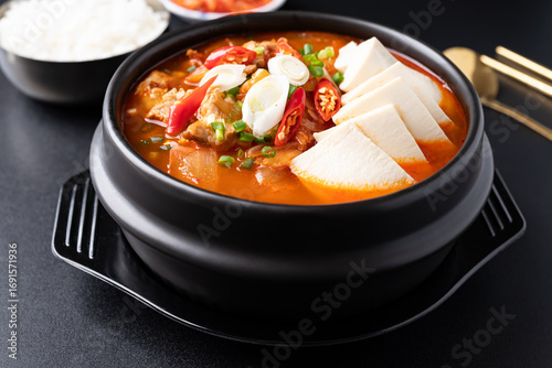 Korean food (Kimchi Jjigae), Kimchi soup with tofu and pork in Korean stone bowl eating with cooked rice and kimchi on black background
