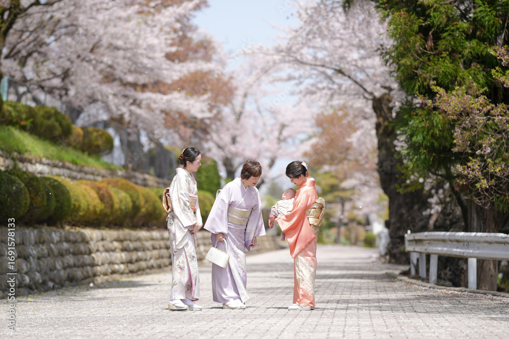 Obraz premium Three women in traditional Japanese clothing are walking down a path. One of the women is holding a baby. The scene is peaceful and serene, with cherry blossoms in the background