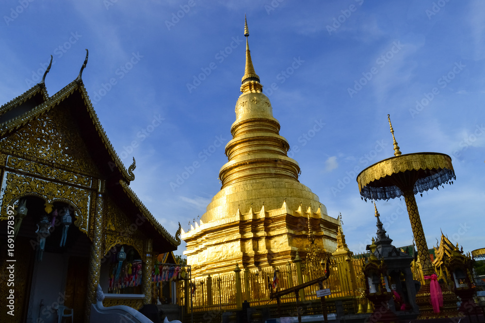 Naklejka premium Church and Golden pagoda in evening, Lanna Architecture, Symbols of Buddhism, South East Asia at wat phra that hariphunchai in Lamphun, north, Thailand