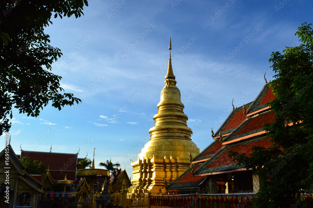 Naklejka premium Church and Golden pagoda in evening, Lanna Architecture, Symbols of Buddhism, South East Asia at wat phra that hariphunchai in Lamphun, north, Thailand