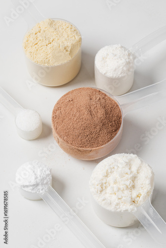 Assorted protein powder and supplement scoops on white marble background for nutrition and fitness