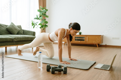 Young Asian woman doing sport exercises indoor. Beautiful girl workout at home. Athletic outfit is doing mountain climber exercises