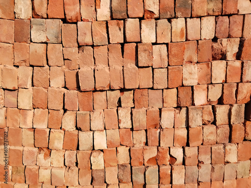 High stack of red bricks arranged in layered pile for construction site storage, traditional Indian building materials in organized bricklaying pattern