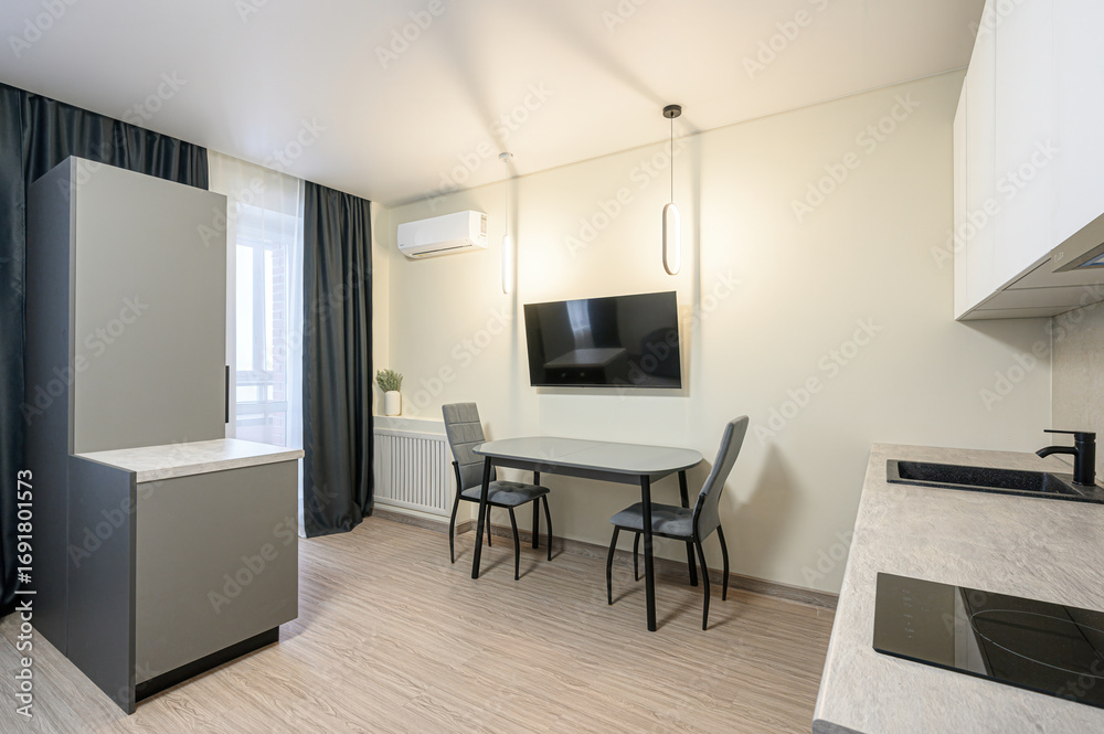 Fototapeta premium well-lit, modern interior. Features a dining area with table, chairs, a wall-mounted TV and a partial view of a kitchen area with sink