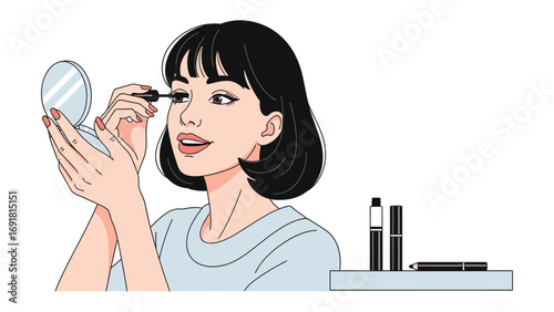Young woman applying mascara to her eyelashes while holding a compact mirror and looking in it with makeup products nearby