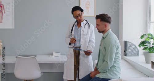 Doctor and patient at clinic or hospital. African woman medic and Caucasian man patient discuss treatment and look at some paper documents such as informed examination consent or medical check results