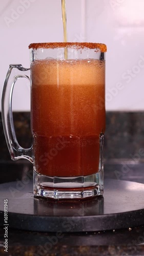 Beer is being poured into a glass mug with a chili powder rim, creating a michelada cocktail