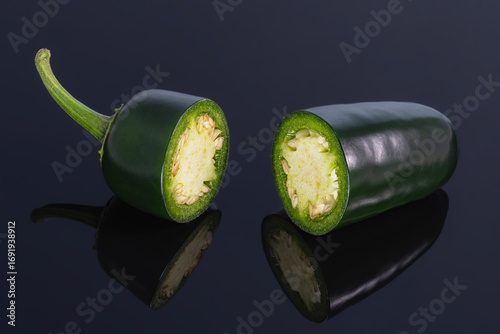 Green jalapeno pepper cut in half on a black background