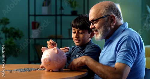 Indian grandfather teaching kid saving money in piggy bank at home, elderly man guiding grandson about financial discipline, inculcating good money habit for secure future, family bonding indoors