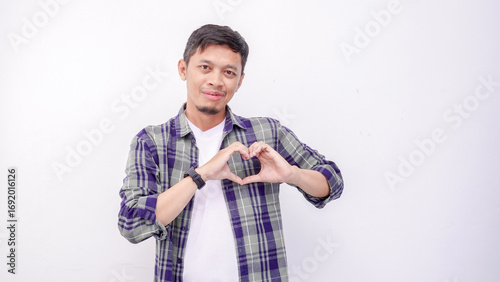 Asian young man smiling while giving heart shape symbol using fingers on white background