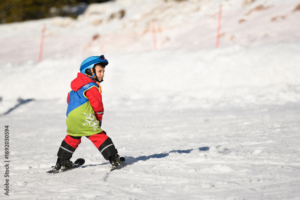 Fototapeta premium Child skiing downhill on sunny winter day