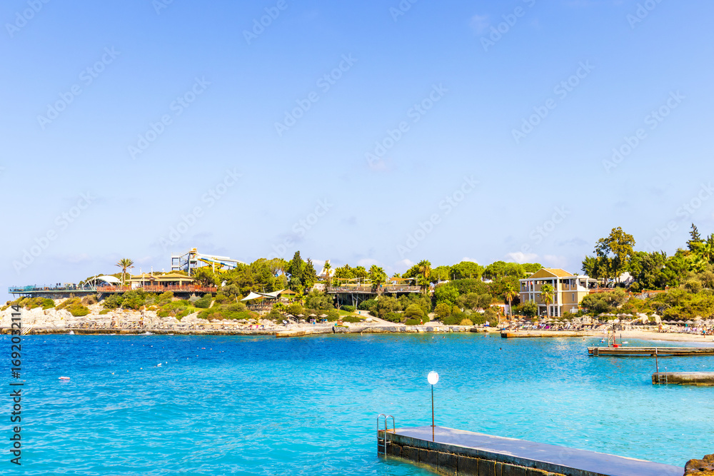 Obraz premium A picturesque seascape with palm trees in the foreground and a rocky coast. Buildings and observation decks are visible on the rock. The azure sea and clear skies create the atmosphere of a resort and