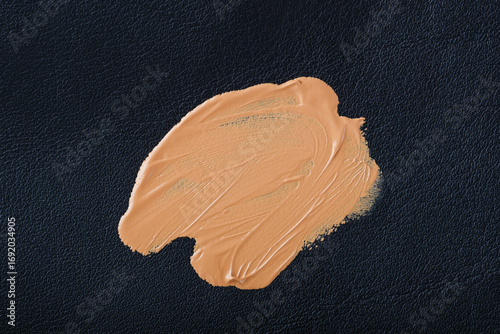 Smudged marks of brown cosmetic substances spread across a textured black leather surface. Daily cosmetic stains foundation on leather upholstery of furniture. top view