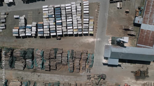 This aerial image captures a top-down view of a timber processing facility, showing perfectly stacked wooden logs and packaged materials.