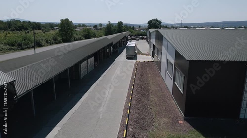 Aerial view of an industrial facility for wood drying and storage, with organized piles of processed wooden poles and sheltered areas. A truck is seen maneuvering through the premises