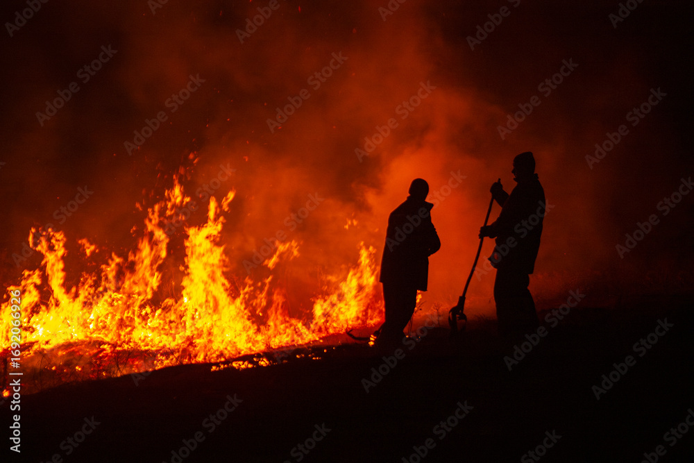 Fototapeta premium Silhouettes of two firefighters against night wildfire