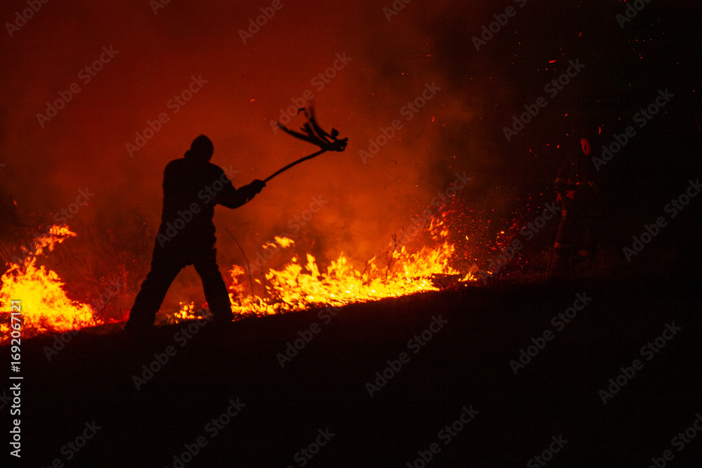 Obraz premium Man fights wildfire at night using improvised tools 