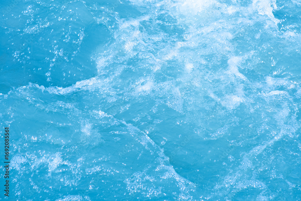 Obraz premium Blue water with ripples on the surface. Defocus blurred transparent blue colored clear calm water surface texture with splashes and bubbles. Water waves with shining pattern texture background.