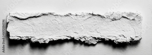 A horizontal, slightly irregular, light-gray, textured slab, like ripped paper or plaster, sits on a plain white surface