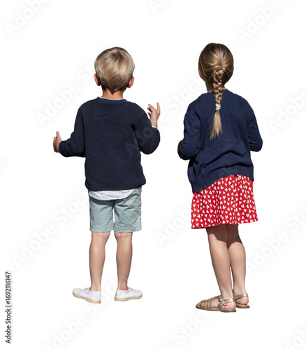 Deux enfants immobiles vus de dos, observant quelque chose devant eux, le petit garçon fait des gestes avec la main, petite fille en jupe rouge à motifs blancs, scène estivale en plein soleil.