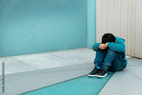 Sad preteen sitting against blue wall feeling alone