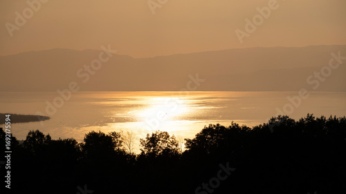 Coucher de soleil sur le lac Léman or brillant depuis la rive française avec vue sur sur la silhouette de la rive suisse. 
